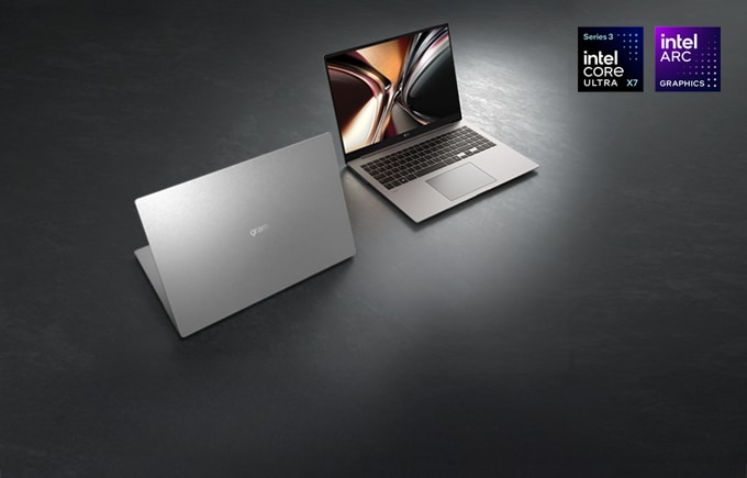 세련된 다크 그레이 톤의 바닥 위에 실버 컬러의 LG 그램 노트북 두 대가 놓여 있으며, 뒤에 배치된 노트북은 화면을 펼쳐 선명한 화질을 보여주고 앞의 노트북은 반쯤 닫힌 상태로 뒷면을 보여주는 이미지